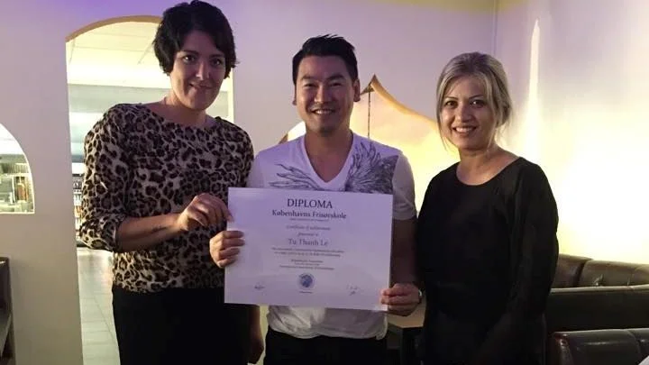 Picture of the owner holding a diploma and 2 hairstylist by his side